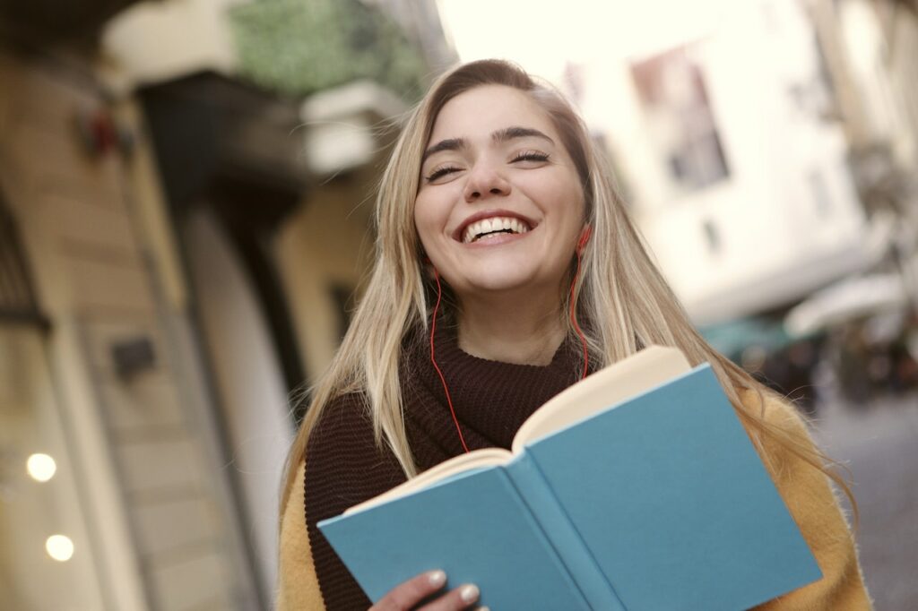 Frau lächelt Buch in der Hand Studentin Mit dem Arbeitspensum an der Universität klar kommen
